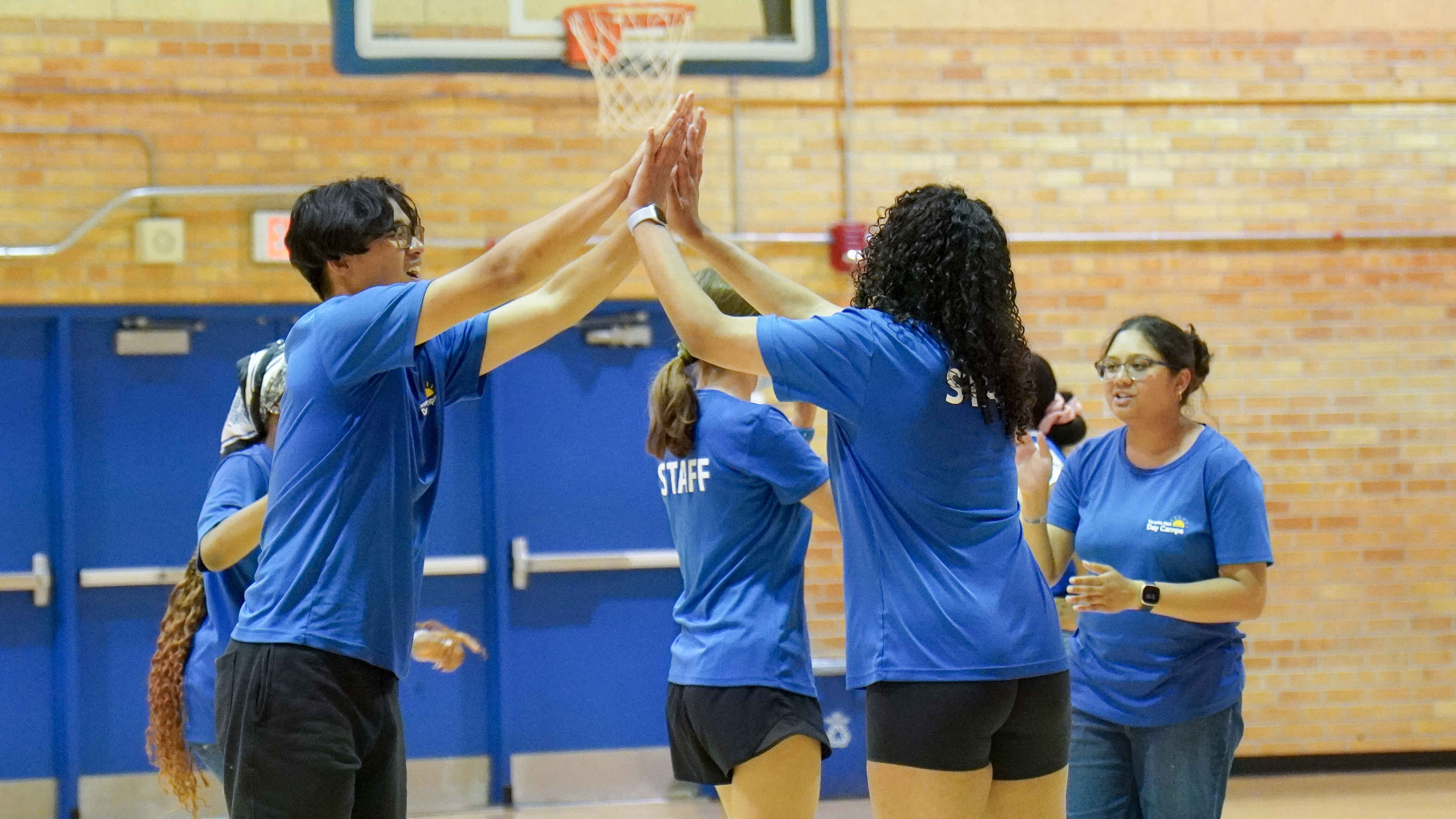 A group of Camp Counsellors share high fives in a gymnasium